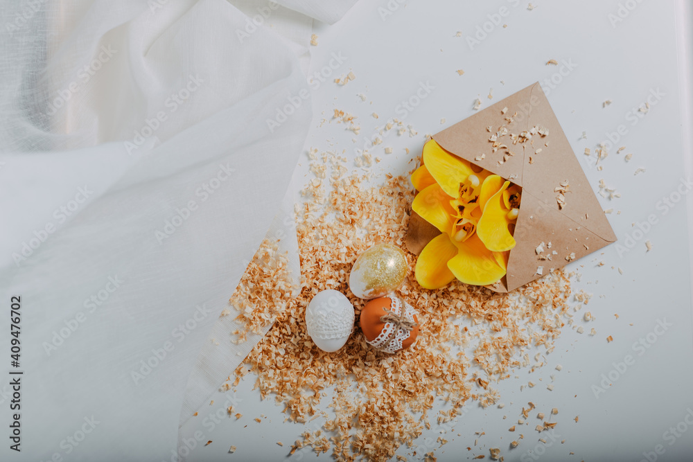 Three easter eggs on white background with sawdust around. Happy Easter card with yellow orchid flowers. Easter eggs decoration with lace border and rope. Golden easter egg. Three easter eggs on white background with sawdust around. Happy Easter card with yellow orchid flowers. Easter eggs decoration with lace border and rope. Golden easter egg.