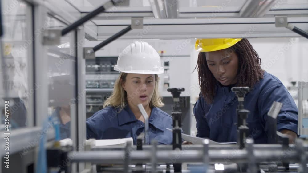 Diverse female factory engineers using paper manual and tablet, studying and testing new industrial machine . Production process or machinery concept
