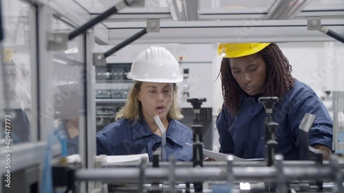 Diverse female factory engineers using paper manual and tablet, studying and testing new industrial machine . Production process or machinery concept