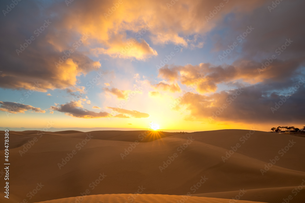 Sunset in the desert, sun and sun rays, dramatic colorful clouds in the sky. Golden sand dunes in the desert in Maspalomas, Gran Canaria, Canary Islands, Spain.