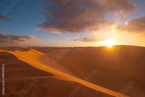 Golden sand dunes in desert in Maspalomas. Sunset in the desert, sun and sunrays, beautiful dramatic clouds and blue sky. Gran Canaria, Canary islands, Spain
