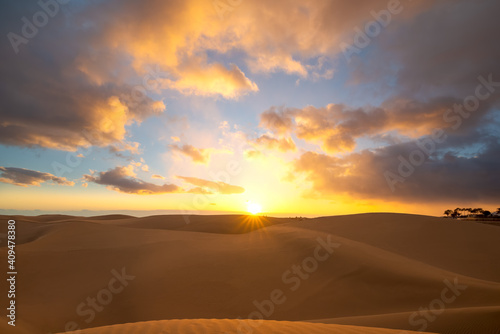 Sunset in the desert, sun and sun rays, dramatic colorful clouds in the sky. Golden sand dunes in the desert in Maspalomas, Gran Canaria, Canary Islands, Spain. © Jordanj