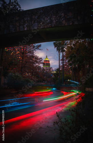 The River Walk in San Antonio, Texas at night with Christmas lights and riverboat neon light trails leading to the Tower Life Building moving forward.