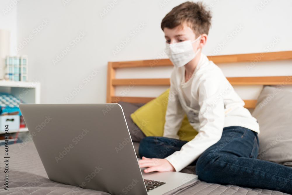 Boy medical mask is watching school lesson laptop, sitting bed on