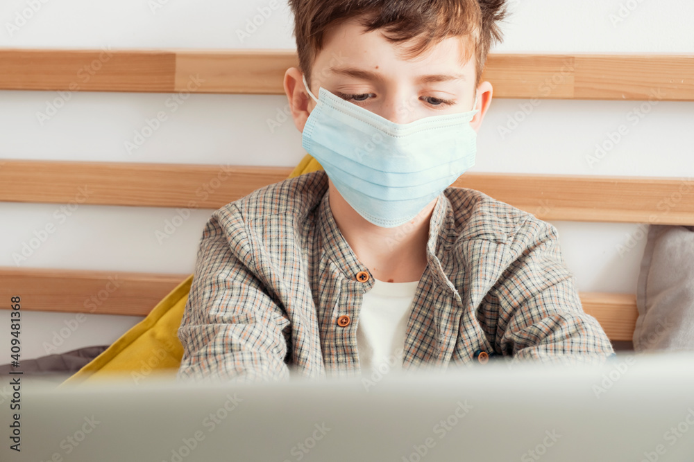 Boy medical mask is watching school lesson tablet, sitting bed on