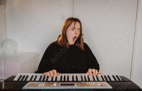 Funny bored teenager girl playing electric synthesizer piano yawning during online lesson at home. Child leisure activity. photo