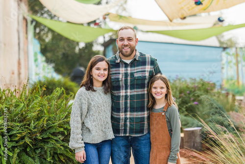 Fototapeta A stepfather with his two step daughters standing outside in a downtown park are