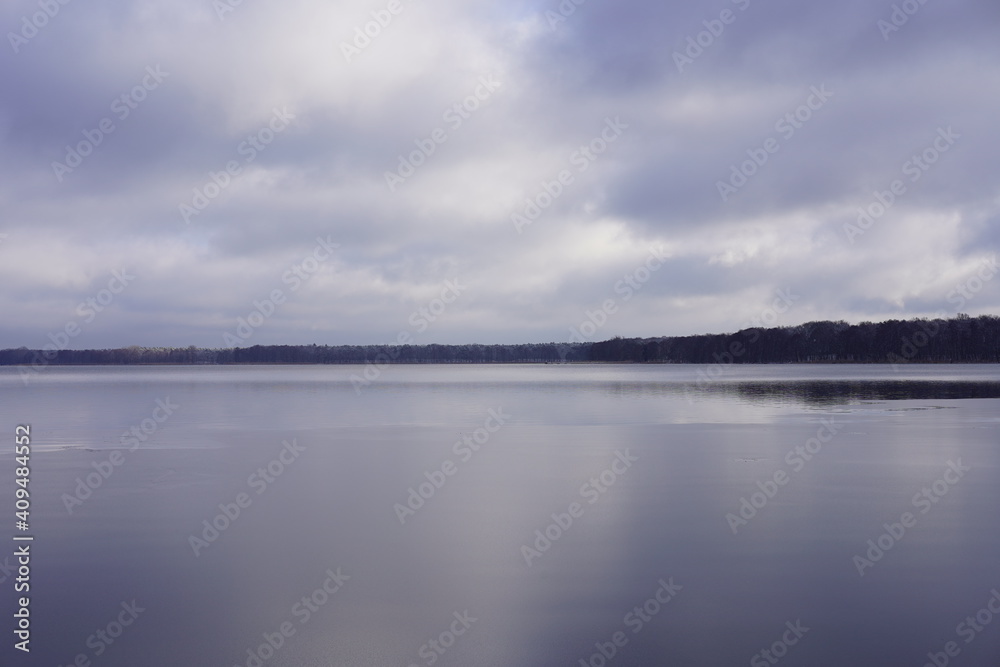 Panoramalandschaft des Müggelsees im Winter mit dünner Eisschicht, Wald und wolkigem Himmel