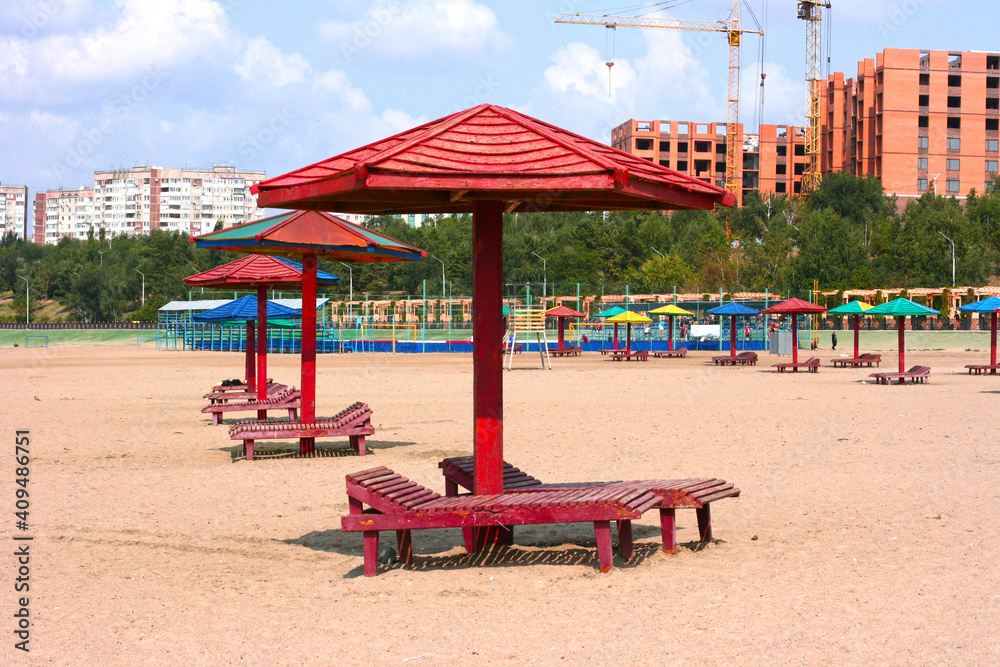 Lounge chairs with and umbrellas on the beach shortly after the beaches reopened following COVID-19 closures. City beach. Empty lounge chairs near water in the sunny day.