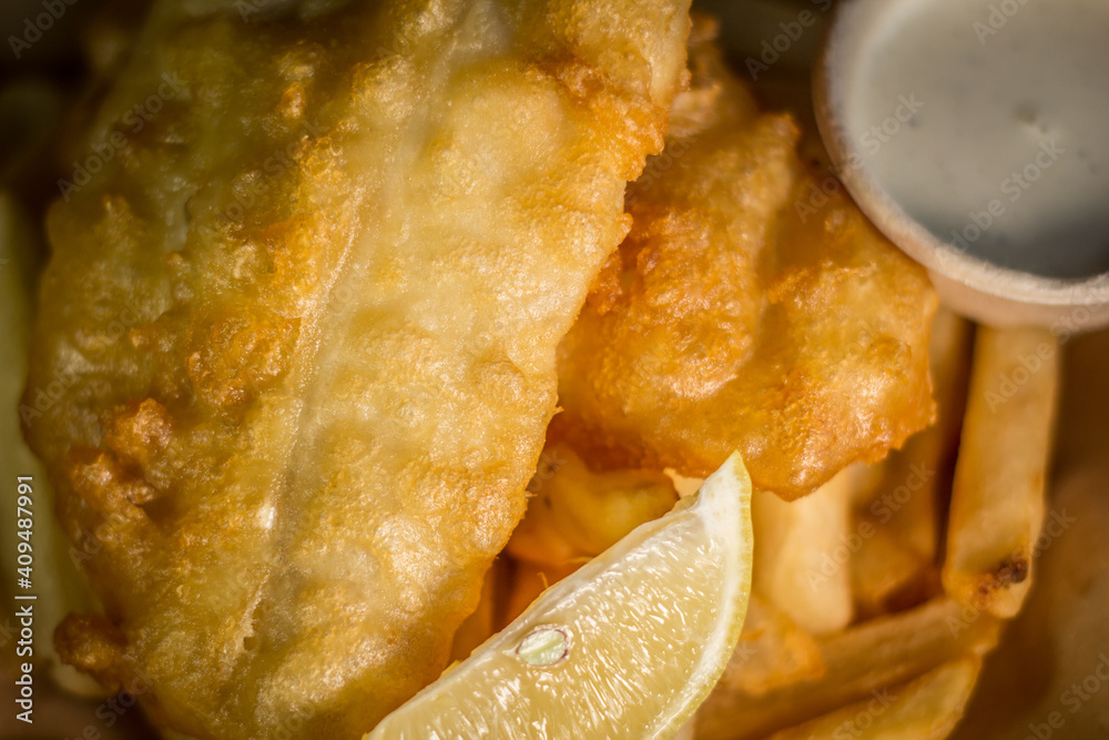 Classic crispy deep fried fish and chips with lemon and tartar sauce white dish on a wooden table Classic crispy deep fried fish and chips with lemon and tartar sauce white dish on a wooden table