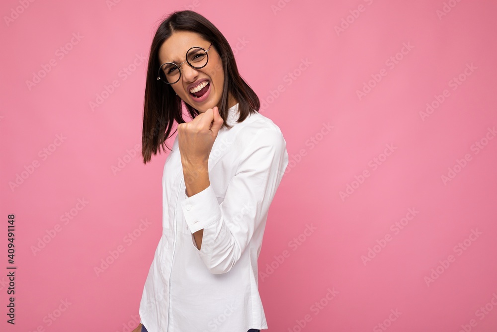 Young positive happy cool beautiful brunet woman wearing white shirt and optical glasses isolated over pink background with empty space and showing rock and roll gesture Young positive happy cool beautiful brunet woman wearing white shirt and optical glasses isolated over pink background with empty space and showing rock and roll gesture