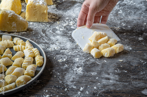 Gnocchi preparation steps: Woman's hand picking up gluten free handmade mashed potato gnocchi using a scraper. Flour sprinkled on a dark table. Creating authentic fresh pasta dough for Italian dish photo