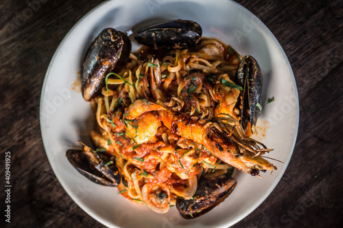 Linguine spaghetti marinara seafood dish with prawn, mussels, parsley, tomato on a white dish and wooden table
