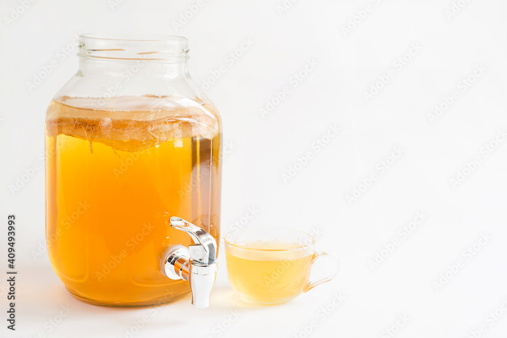 Kombucha-a drink made from tea mushroom in a glass jar with a tap. Transparent mug with a yeast drink made from a Japanese mushroom-jellyfish. White background, healthy food. Copy space Kombucha-a drink made from tea mushroom in a glass jar with a tap. Transparent mug with a yeast drink made from a Japanese mushroom-jellyfish. White background, healthy food. Copy space