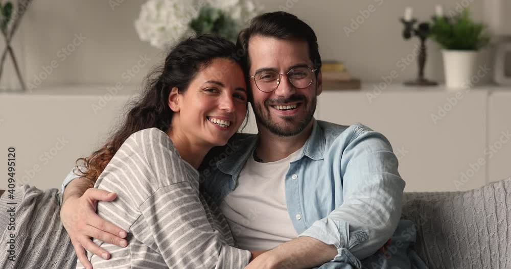 Happy young couple in love portrait concept. Spouses hugging relax on sofa smile look at camera. Homeowners rest in first modern apartment, rented flat, tenancy, bank loan, romantic relations concept Happy young couple in love portrait concept. Spouses hugging relax on sofa smile look at camera. Homeowners rest in first modern apartment, rented flat, tenancy, bank loan, romantic relations concept
