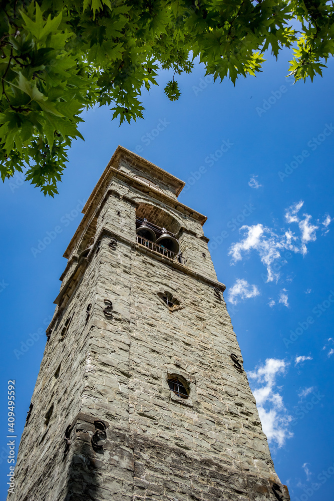 Spring street low angle view, stone bell tower, tree branch and sky from town of Metsovo, Epirus, Greece. The establishment is popular winter ski Greek resort with old Balkans style houses