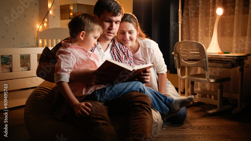 Happy family with little boy reading book at night before going to sleep. Concept of child education and family having time together at night.