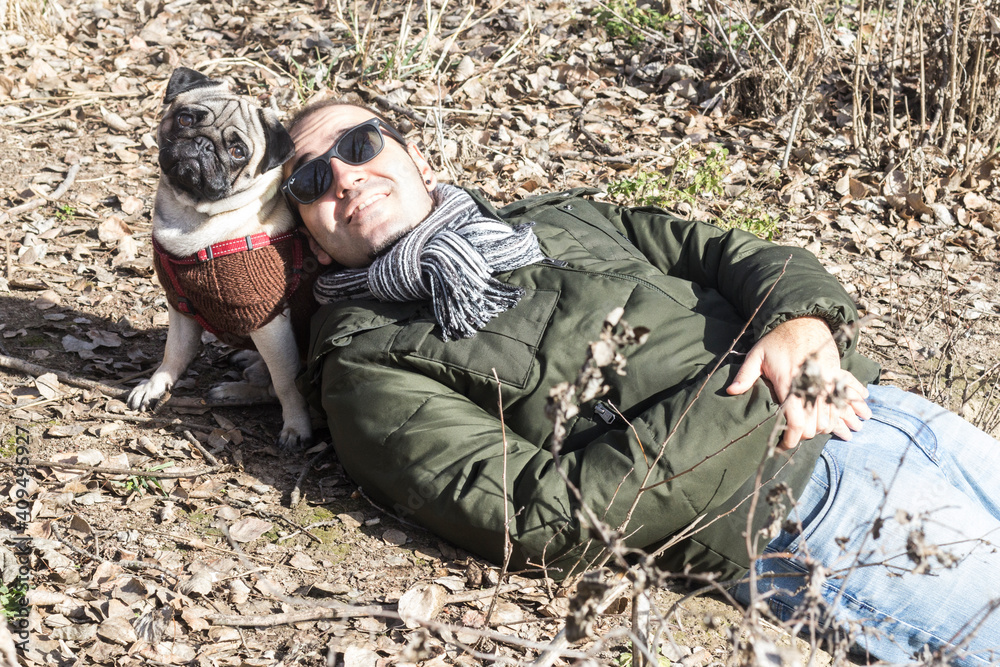 
Young boy in sunglasses lying in the field with his pug dog looking at the camera