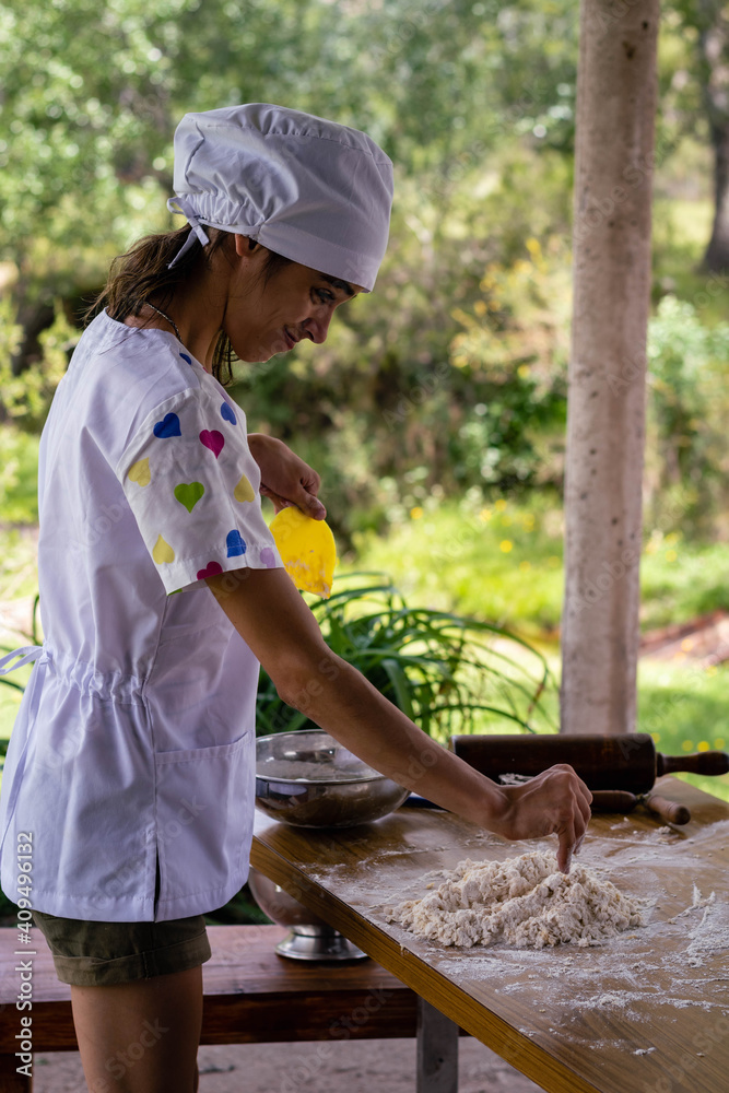 Obraz premium young woman dressed as a bakery making bread with flour eggs background green field with sun on vacations cordoba argentina