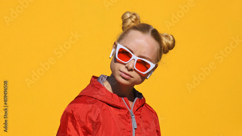 Portrait of happy teenager blonde girl in headphones sunglasses listens to music on smartphone, smiles, dances, shaking her head rhythmically against yellow background in summer. Emotions