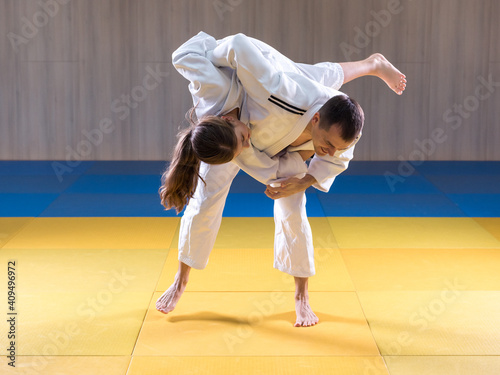 Adult male judoka throwing young female judo girl with hip throw photo