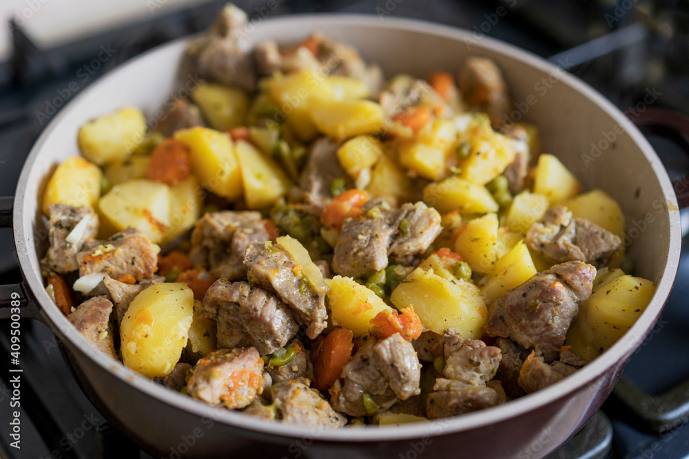Meat stewed with potatoes, carrots, vegetables and spices in a pan. Process of cooking dish in a kitchen. Selective focus with copy space Meat stewed with potatoes, carrots, vegetables and spices in a pan. Process of cooking dish in a kitchen. Selective focus with copy space