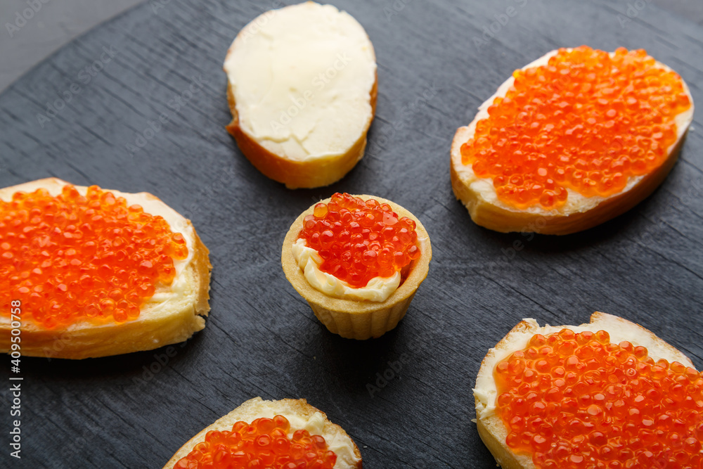 Canapes with butter and red caviar on a black board on a concrete background. Canapes with butter and red caviar on a black board on a concrete background.