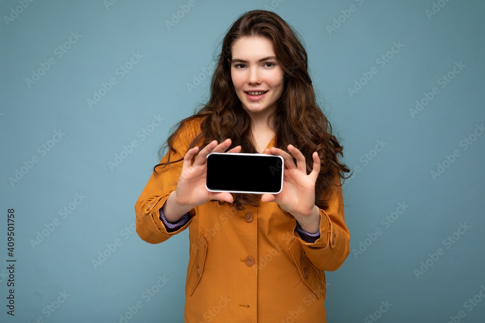 Photo of beautiful smiling young woman good looking wearing casual stylish outfit standing isolated on background with copy space holding smartphone showing phone in hand with empty screen display for