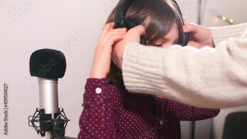 Long hair teenager prepares to record a song. The teacher puts headphones on his head. Creative realisation of a child in music education. He shows like. photo