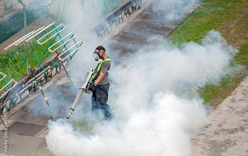 Healthcare worker using Fogging machine spraying chemical to eliminate mosquitoes and kill larvae to fight against the spread of dengue fever, Zika virus or Malaria at a residential area.