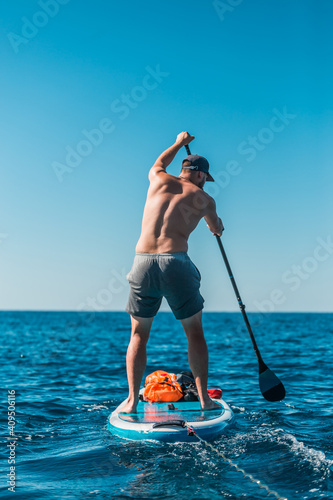 Valokuva Young athletic man paddling on a SUP stand up paddle board in blue water sea in