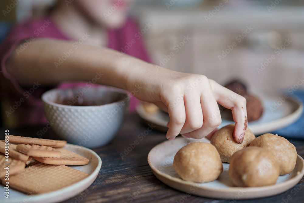 Child hands making sweet balls cookies called Potato of marzipan, biscuits, cocoa. Process of dessert cooking, wooden table with ingredients. Selective focus, copy space