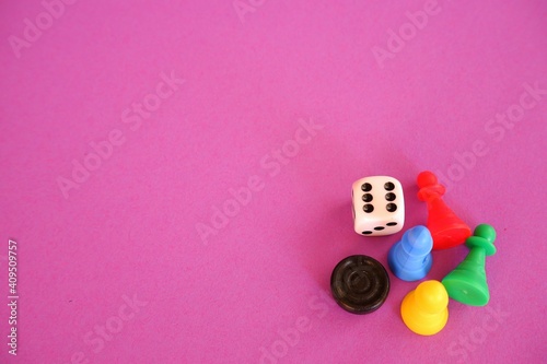 Different colored board game figures and dices in the right corner of the purple pink wallpaper background