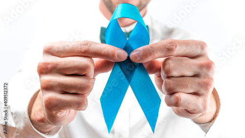 Men cancer. Hipster man in bright shirt, cyan bowtie with blue ribbon in hands on white background. Awareness prostate of health in November. Adrenocortical carcinoma concept.