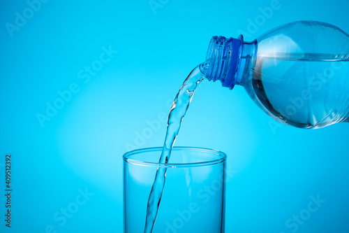 In an empty glass, pour fresh water on a blue background. Side view with copy space. The concept of drinks.