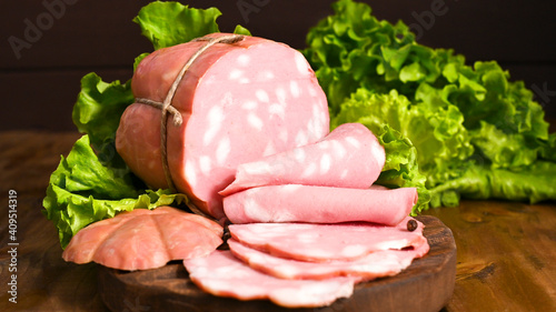 Italian Whole block of mortadella on a wooden plate decorated with green salad. Traditional big sausage and black pepper pistachios Region Emilia Romagna and the city of Bologna. Copy space.