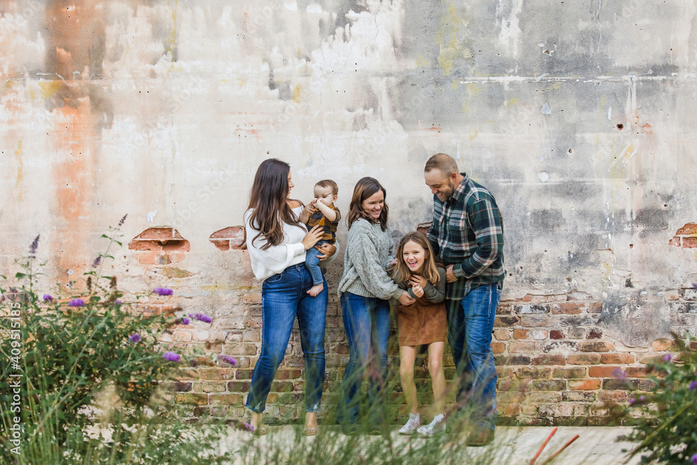 A fun family of five with two girls and a baby boy standing by an urban old brick wall A fun family of five with two girls and a baby boy standing by an urban old brick wall