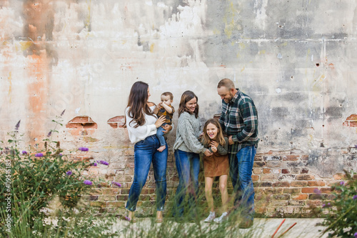 A fun family of five with two girls and a baby boy standing by an urban old brick wall