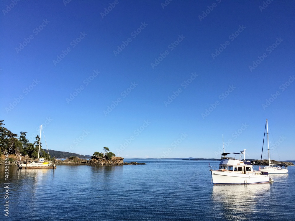 The beautiful vistas of boats anchored off of Portland Island, in the Gulf Islands of British Columbia, Canada.  The ocean and sky create a fully blue background.