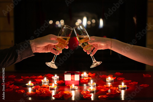 Couple in love toasting together with glasses of champagne to celebrate Valentine’s Day during romantic dinner. Red roses, gifts and flowers. Concept about lifestyle, celebrations and people.