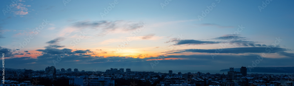 Early morning winter sky just before the sunrise over small seashore town. Golden dawn lights up in the sky over a sleeping city. Panoramic landscape with urban skyline.