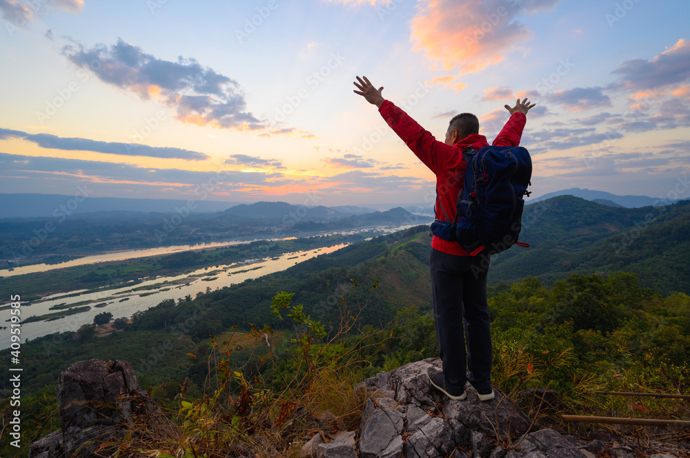 Senior man standing the cliff open arms enjoying the view of Mekong river at sunrise at phu pha dak in nong khai, Thailand