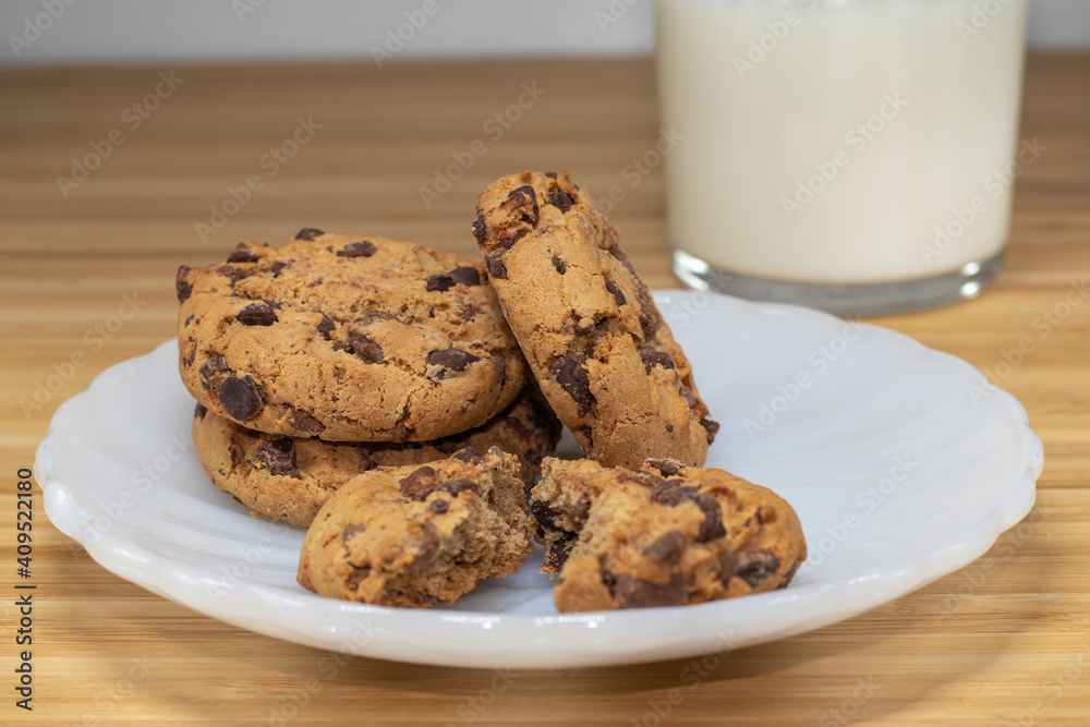 Chocolate chip cookies with glass of milk in the background, on a wooden table. Chocolate chip cookies with glass of milk in the background, on a wooden table.