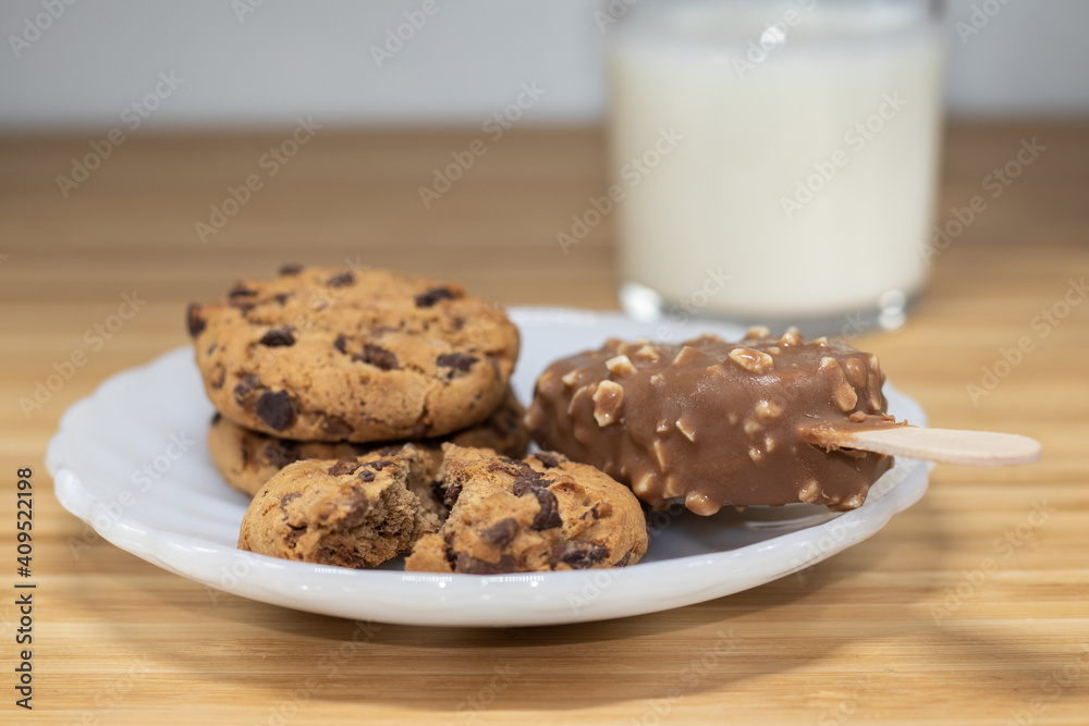 Chocolate chip cookies with a ice cream stick of a chocolate and almonds and a glass of milk in the brackground Chocolate chip cookies with a ice cream stick of a chocolate and almonds and a glass of milk in the brackground