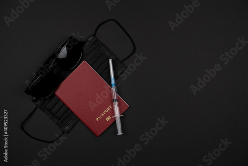 On a black background, a passport, black glasses, a black medical mask and a syringe. Quarantine travel concept