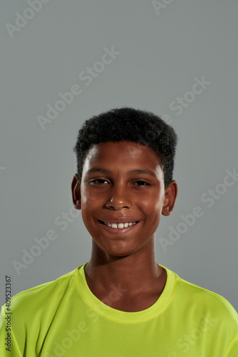 Close up portrait of a cheerful happy teenage african boy smiling at camera while posing isolated over grey background
