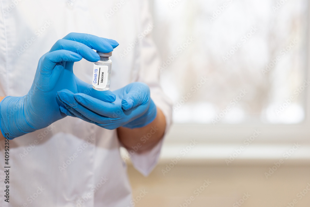 The hands of a doctor or nurse are carefully holding a bottle of coronavirus vaccine. The hands of a doctor or nurse are carefully holding a bottle of coronavirus vaccine.