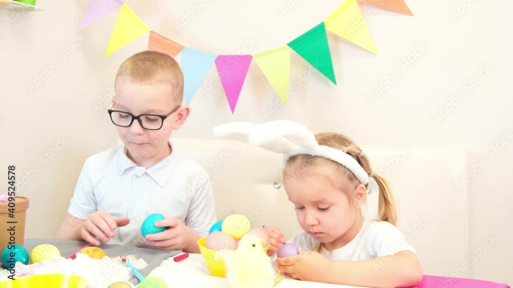 Funny kids in bunny ears draws eggs for Easter day. Children eat sweets and laugh. Funny kids in bunny ears draws eggs for Easter day. Children eat sweets and laugh.