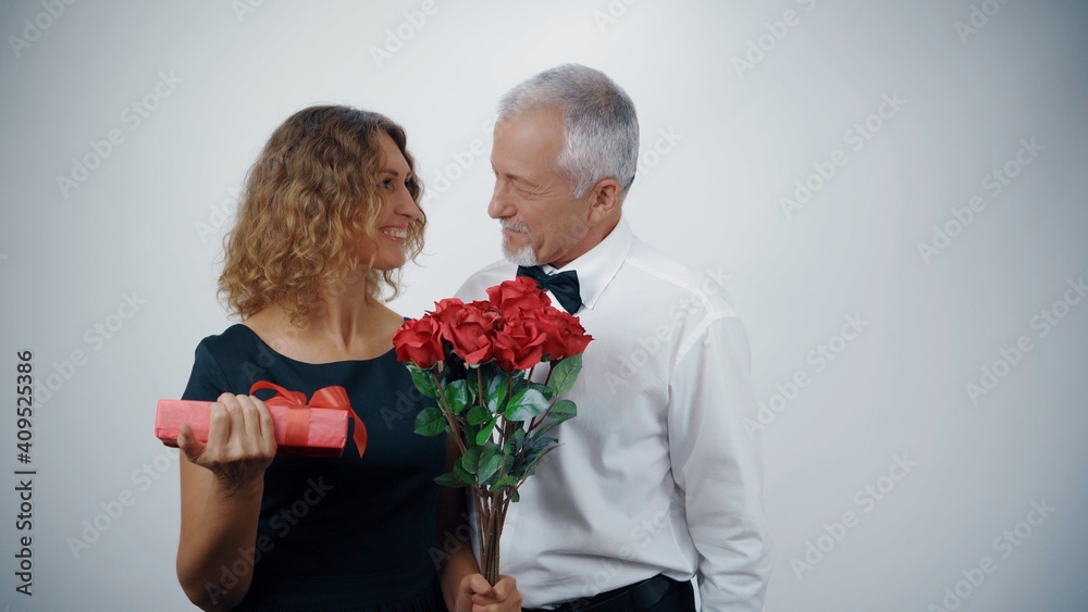 A loving elderly husband presents a gift and roses to a mature smiling woman. A loving elderly husband presents a gift and roses to a mature smiling woman.