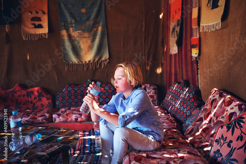 Valokuva young thirsty boy drinking water from PET bottles in bedouin tent, travelling th